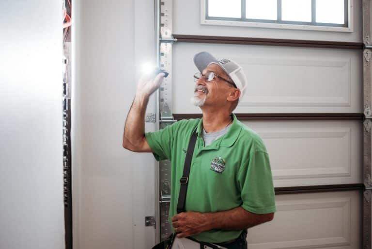 Inspection Gator inspector in a green shirt and white cap looking up and examining a white garage door