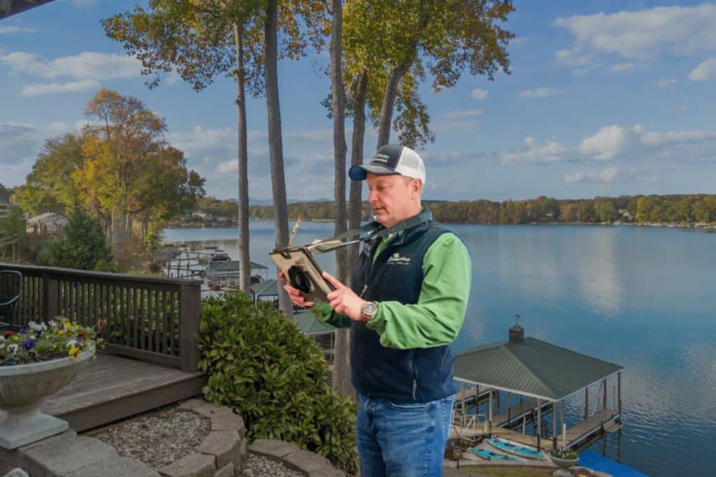 Home inspector reviewing a tablet on the deck of a lakefront property with a private dock and boathouse
