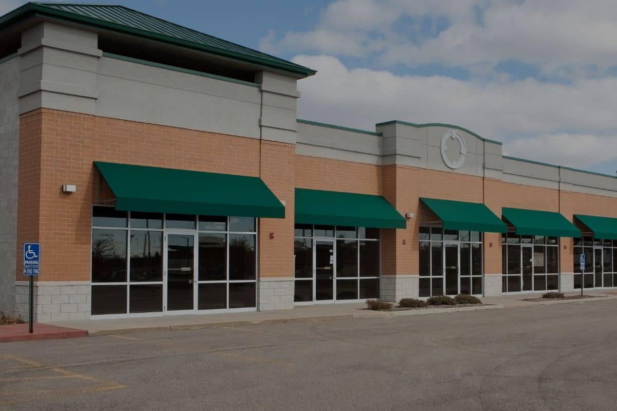 Multi-tenant retail strip center with green awnings and parking lot, a common commercial property investment
